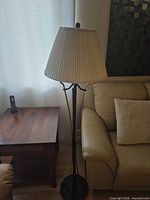 Full view of black metal floor lamp with cream pleated shade beside sofa