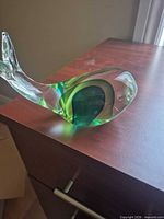 Side view of clear and green glass whale on wooden surface