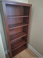 Full view of tall brown five-shelf bookcase in corner