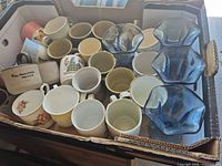 Box showing mixed ceramic mugs and blue glass tumblers