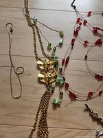 Group of necklaces showing gold-tone leaf pendant necklace, silver-tone snake chain, red bead necklace