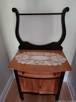 Full view of washstand showing two-tone wood, backsplash rail, drawer, cabinet doors, casters