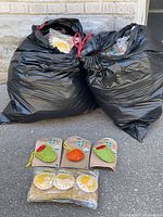 Two large garbage bags filled with packaged Loofah-Art scrubbers; several examples displayed in front
