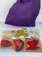 Front view of six packaged novelty loofah scrubbers with purple bag behind