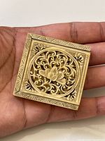 Top view of carved puzzle box in hand showing scale and floral open-work design