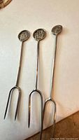 Three silver cocktail picks showing Chinese character finials