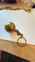 Full view of brass spherical coin holder attached to chain and ring