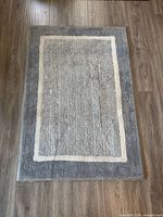 Full view of rectangular gray rug with cream border on wood floor