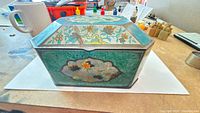 Front and side view of turquoise floral painted metal tin with hinged lid