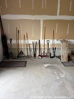Row of assorted long-handled tools against drywall wall