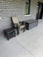 Stack of five beige sling chairs beside resin wicker cube side table and dark grey deck box