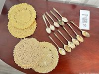Group of 11 silver-plated spoons and approx 8 gold doilies on tabletop