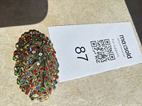 Front view showing gold-tone leaf design with multicolor rhinestones