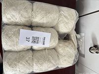 Bag containing eight cream yarn skeins with MaxSold lot tag