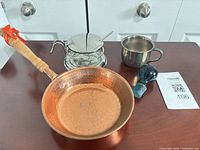 Group shot showing copper pan, condiment jar in stand, silver cup, blue stopper