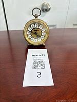 Front view of Forestville brass wind-up alarm desk clock showing dial and feet