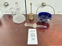 All four items grouped on tabletop: cruet, brass bell, cobalt bowl in basket, glass percolator stem