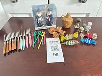 Group shot of entire lot on table showing forks, sword picks, box of wizard shakers, glass candies, wood cups, thimbles, ceramic jug