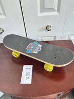 Full skateboard on table, grip tape side up, shows yellow wheels
