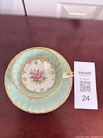 Teacup resting in saucer showing interior pink rose motif, seafoam border and gold trim