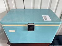Front view of light blue/teal Coleman steel cooler with cream stripe and chrome latch