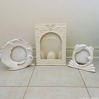 Front view of three white frames: rectangular arched, round swan motif, round leaf motif