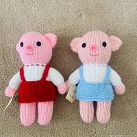 Front view of two knitted pig dolls in red and blue outfits