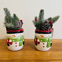 Front view of both ceramic snowman planters with greenery