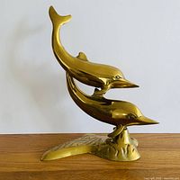 Front view of polished brass two-dolphin sculpture on base