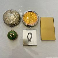 Five vanity items arranged: two round compacts, mini green pill box, two rectangular card holders