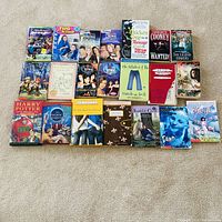 Overhead view of 22 assorted children and teen fiction books arranged in two rows on carpet; shows titles including Harry Potter, Charmed series, Mary-Kate & Ashley, Sisterhood of the Traveling Pants, Chicken Soup for the Teenage Soul, Percy Jackson, Eragon, Baby-sitters Club