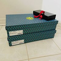 Stacked two patterned Tory Burch boxes with black Tip Top Tailors box on top