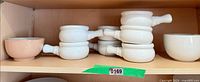 Shelf view showing eight white handled crocks and one peach bowl