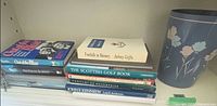 Stack of assorted books alongside blue floral waste basket