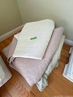 Stacked bedding showing white mattress pad, pink quilted coverlet, green sheets
