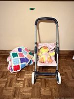 Front view of doll stroller with plush duck strapped in and crochet blanket beside