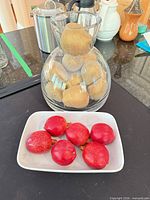 Faux kiwis in clear glass vase, faux pomegranates on white platter