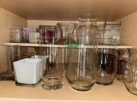 cabinet shelf showing assorted clear, white and colored glass vases of different shapes