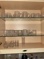 Cabinet view showing handled mugs on upper shelf, cut-pattern rocks glasses on middle shelf, rounded stemless wine glasses and tall highball on lower shelf