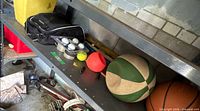 Shelf with golf cart frame, black bag, golf balls, basketballs, bats visible