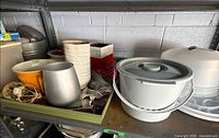 Shelf view showing vases, yellow bowl, silver vase, white plastic bucket, cake carrier and tins