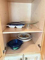 Cabinet shelves showing majority of items: blue casserole, scenic bowl, divided dishes, glass cake stand