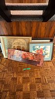 Group of four framed prints leaning against wall showing child portrait, architectural print, still life fruit print, additional print partially hidden
