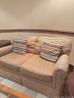 Front view of tan loveseat with two chevron pillows