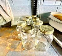 Eight clear glass Mason jars with gold lids on shelving