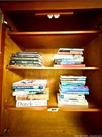Multiple stacks of books on cabinet shelves showing mix of hardcovers and paperbacks