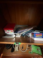 Shelf with ho-ho gift box, paper stacks, Christmas Charades Game, cables, power strip visible