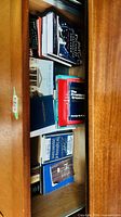 Drawer with multiple stacked books showing mix of formats and visible titles