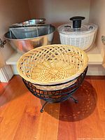 Stainless bowls, mesh strainer, salad spinner, wire stand with wicker basket inside cabinet