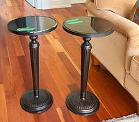 Two matching dark metal pedestal tables with black stone tops